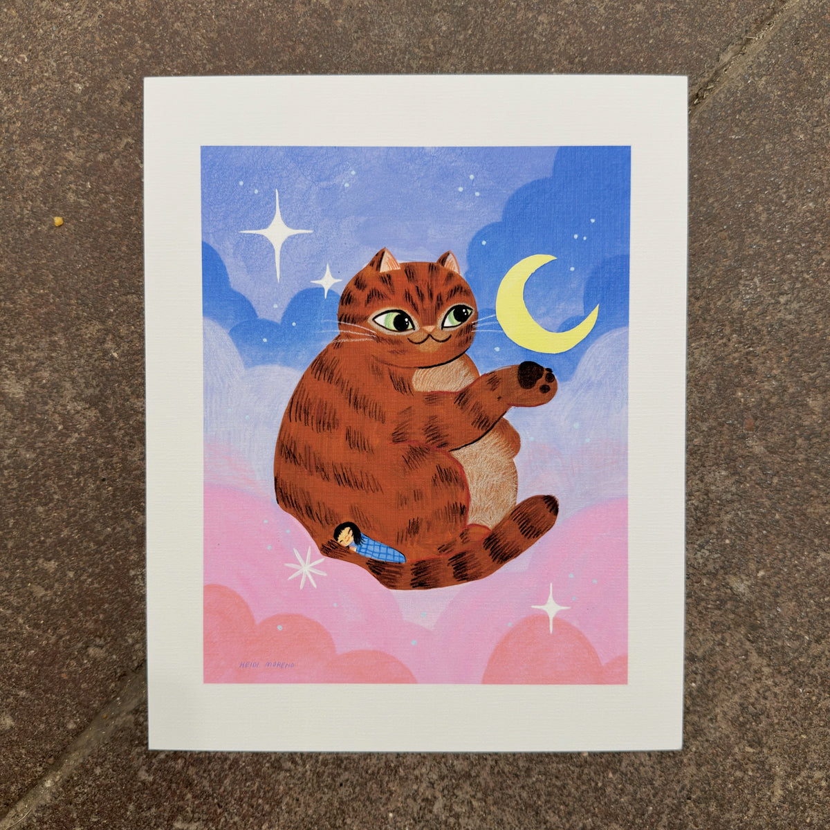 Giant orange tabby cat floating in pink and blue clouds reaching for a crescent moon with a tiny sleeping girl curled in its tail, art print by Heidi Moreno on display at We Are 1976