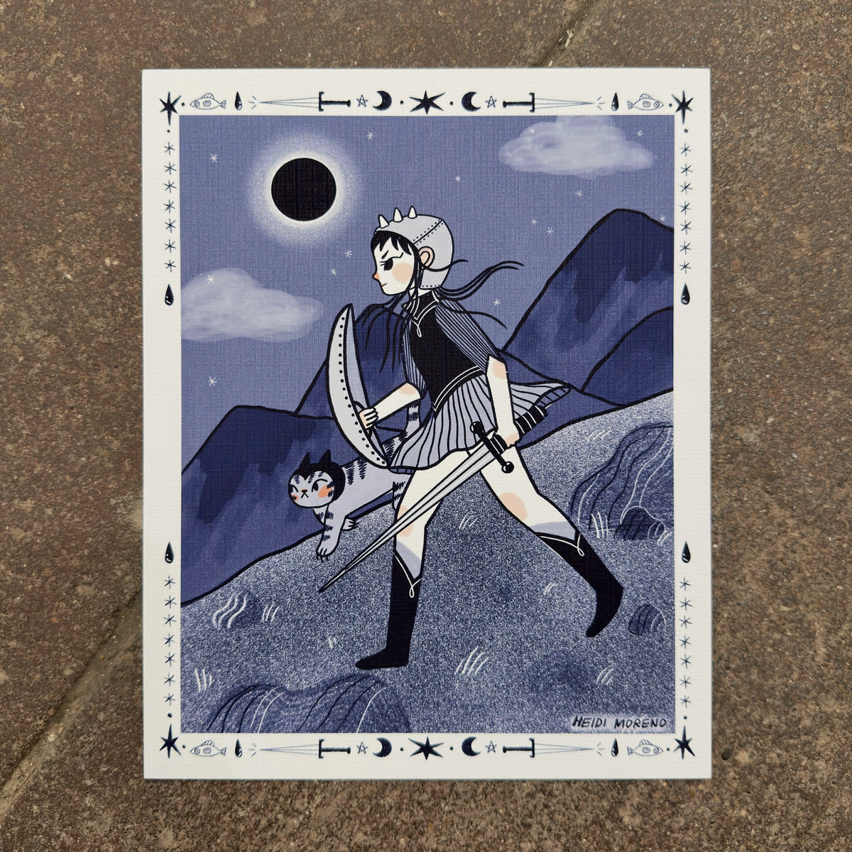 Young warrior with a shield and sword walking with a tabby cat under a total solar eclipse in indigo tones with a tarot-style border, art print by Heidi Moreno on display at We Are 1976
