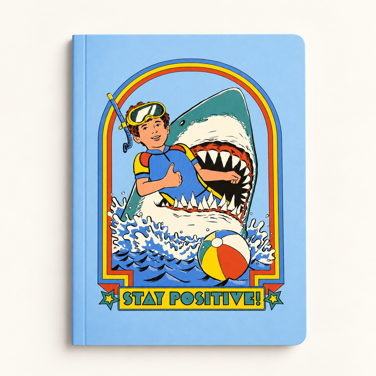 Stay Positive Paperback Notebook (A5) by Steven Rhodes: sky-blue cover with a smiling boy in a snorkel mask giving a thumbs-up as a great white shark bursts from the waves behind him, framed by a retro red and yellow arch above a Stay Positive! banner