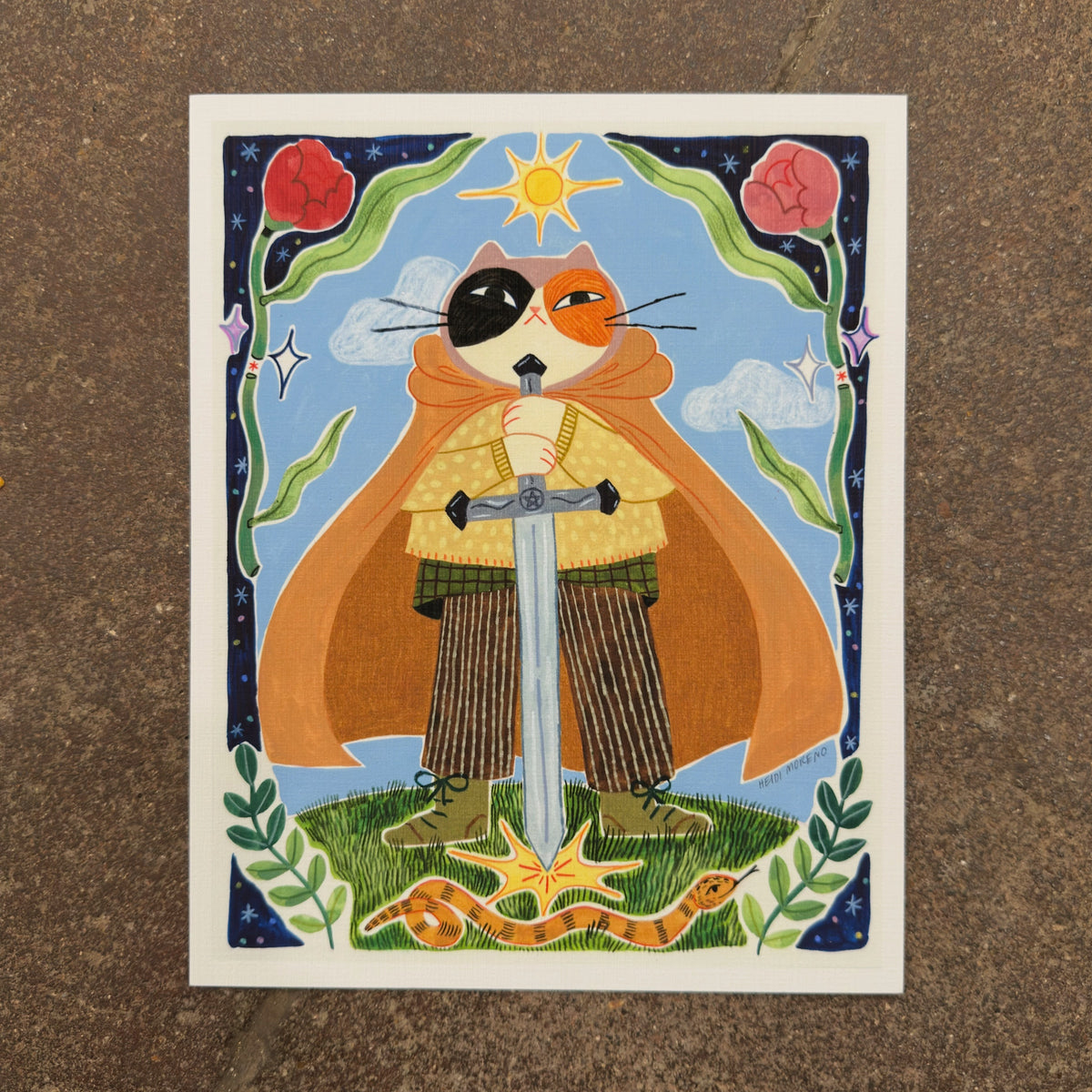 Calico cat in an orange cape holding a large sword planted in the grass with a sun above, a snake below and a border of roses and stars, art print by Heidi Moreno on display at We Are 1976
