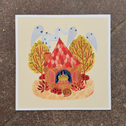 Toad in a party hat looking out the window of a red-roofed cottage with ghosts in the chimney smoke, autumn trees and a sleeping cat, art print by Heidi Moreno on display at We Are 1976
