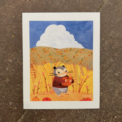 Opossum in a maroon sweater hugging a pumpkin in tall golden grass with pumpkin-dotted hills and a white cloud, art print by Heidi Moreno on display at We Are 1976