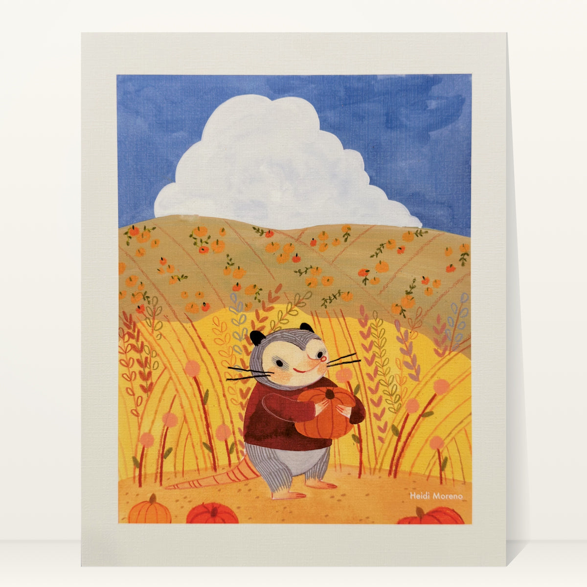 Opossum in a maroon sweater hugging a pumpkin in tall golden grass with pumpkin-dotted hills and a white cloud, art print by Heidi Moreno