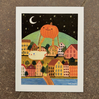 Giant smiling pumpkin on long striped legs walking over a colorful hillside town at night with a small ghost and a crescent moon, art print by Heidi Moreno on display at We Are 1976