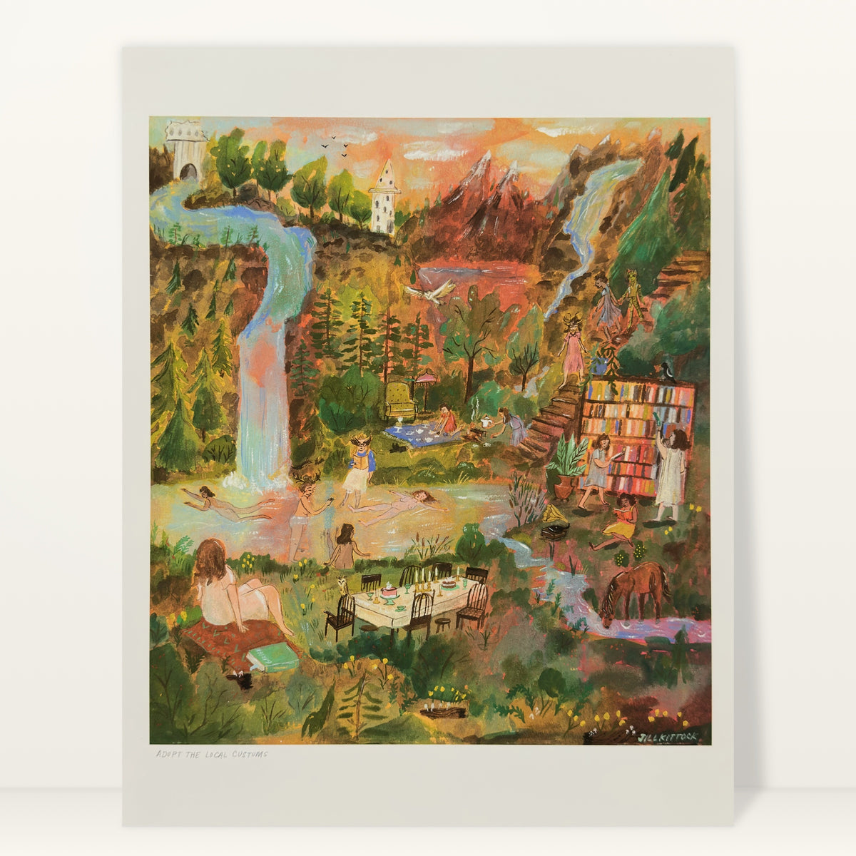 Adopt the Local Customs art print by Jill Kittock against a light studio wall: a fantasy valley with a waterfall, a white tower, swimmers and an outdoor bookcase
