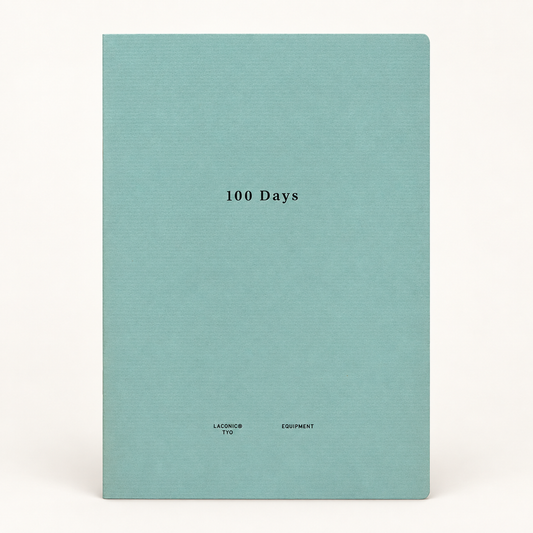 A hardcover notebook or journal with a textured light teal cover, featuring the title '100 Days' printed in black serif font in the center, and 'LACONIC EQUIPMENT' printed at the bottom. The notebook is photographed against a clean, off-white background.
