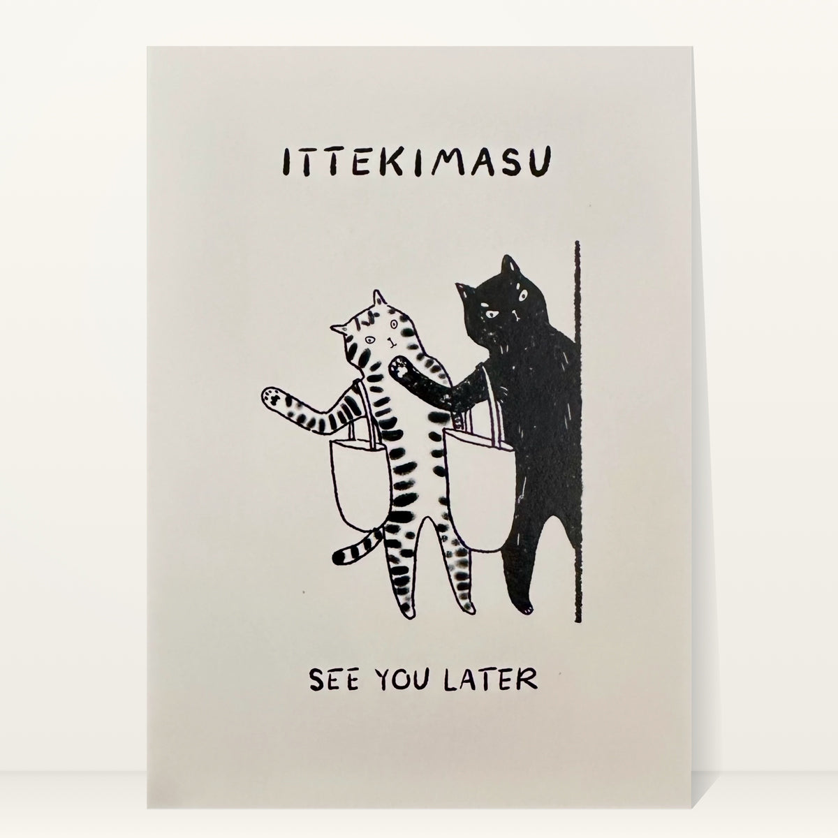 Ittekimasu mini art print by Linnan Ye: tabby cat and black cat with tote bags heading out a door, with the words “Ittekimasu” and “See you later”