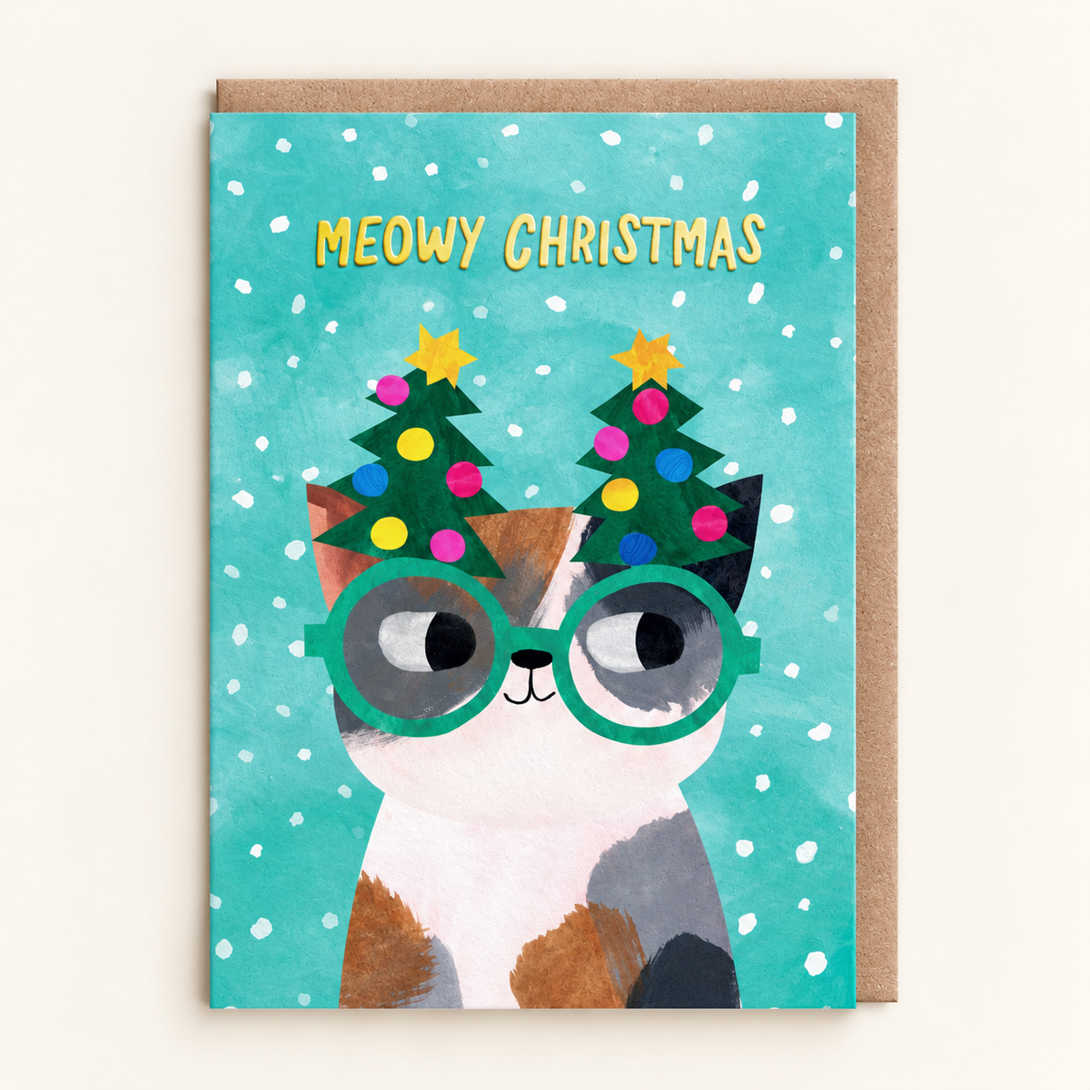 Tree Glasses Kitty Christmas Card by Angela Rozelaar: painted calico cat in green novelty glasses topped with Christmas trees under gold Meowy Christmas lettering on snowy teal, with a brown kraft envelope