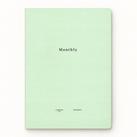 A mint green hardcover notebook with a subtle horizontal ribbed texture, featuring the word 'Monthly' printed in black serif font in the center and small text at the bottom.
