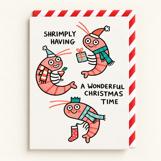 Shrimply Wonderful Christmas Card by Gemma Correll: three cartoon shrimp in hats and scarves with the words Shrimply having a wonderful Christmas time, with a red and white striped envelope