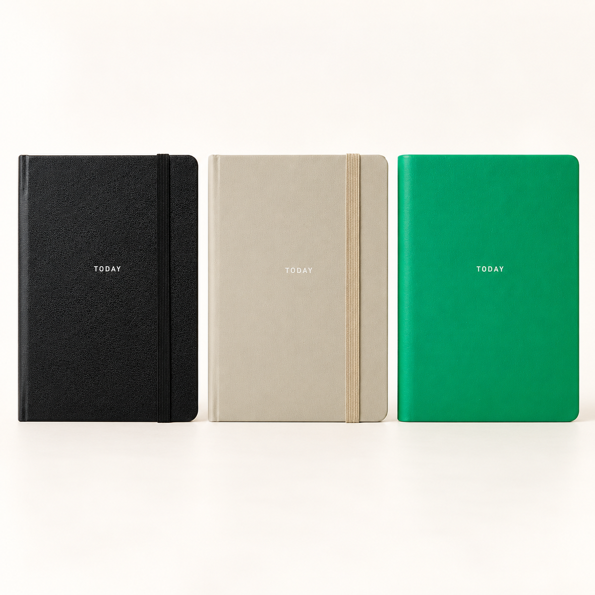 Three slim hardcover notebooks or planners standing upright side by side on a white surface against a white background. The left notebook is black, the middle is light beige, and the right is bright green.